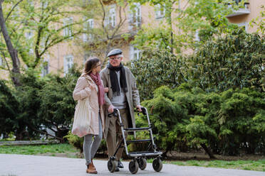 Ein älterer Mann mit Rollator und erwachsener Tochter bei einem Spaziergang im Park. - HPIF03810