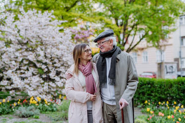 A happy senior man with walking stick and adult daughter outdoors on a walk in park. - HPIF03812