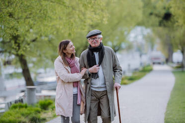 A happy senior man with walking stick and adult daughter outdoors on a walk in park. - HPIF03816