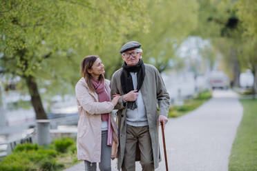 Ein glücklicher älterer Mann mit Spazierstock und erwachsener Tochter im Freien bei einem Spaziergang im Park. - HPIF03816