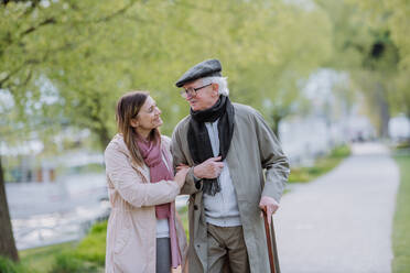 A happy senior man with walking stick and adult daughter outdoors on a walk in park. - HPIF03817