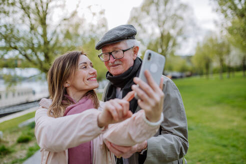 Ein glücklicher älterer Mann und seine erwachsene Tochter machen ein Selfie im Freien bei einem Spaziergang im Park. - HPIF03818
