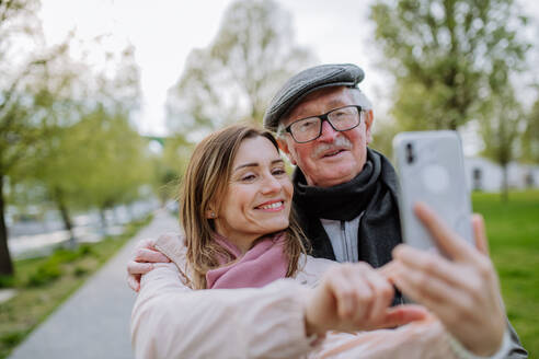 Ein glücklicher älterer Mann und seine erwachsene Tochter machen ein Selfie im Freien bei einem Spaziergang im Park. - HPIF03820