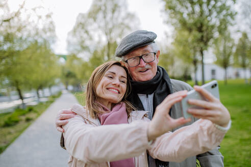 Ein glücklicher älterer Mann und seine erwachsene Tochter machen ein Selfie im Freien bei einem Spaziergang im Park. - HPIF03821