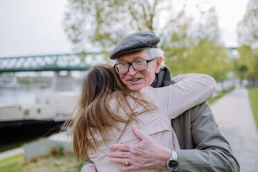 Eine Rückansicht einer erwachsenen Tochter, die ihren älteren Vater umarmt, als sie ihn auf der Straße trifft. - HPIF03823