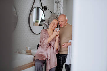 Ein verliebtes älteres Paar im Badezimmer, das ein Smartphone benutzt, Konzept der Morgenroutine. - HPIF03852