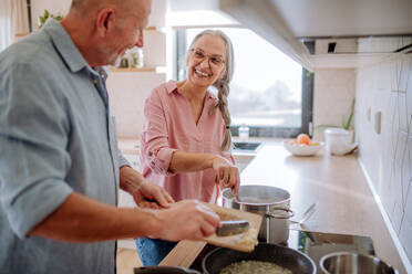 Ein älteres Ehepaar kocht und lächelt gemeinsam zu Hause. - HPIF03873