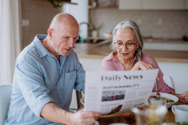 Ein glückliches älteres Ehepaar, das zu Hause frühstückt und gemeinsam Zeitung liest. - HPIF03875
