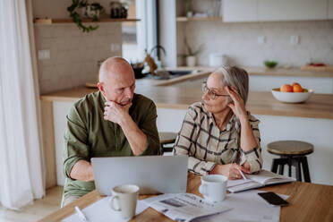 A stressed and sad senior couple calculate expenses or planning budget together at home. - HPIF03886