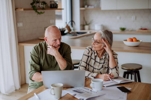 Ein gestresstes und trauriges Seniorenpaar berechnet zu Hause gemeinsam die Ausgaben oder plant das Budget. - HPIF03886