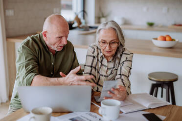 A stressed and sad senior couple calculate expenses or planning budget together at home. - HPIF03890
