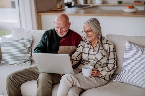 Ein älteres Paar sitzt auf dem Sofa und kauft mit einem Laptop online ein. - HPIF03896