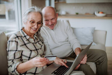 A senior couple sitting on sofa and shopping online with laptop and credit card - HPIF03900