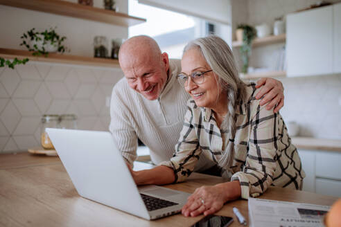 Ein glückliches Seniorenpaar kalkuliert zu Hause gemeinsam Ausgaben oder plant das Budget. - HPIF03901