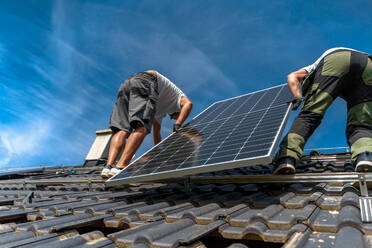 Männliche Arbeiter bei der Installation von Solarpaneelen auf einem Dach, alternative Energie, Ressourcenschonung und nachhaltiger Lebensstil. - HPIF03943