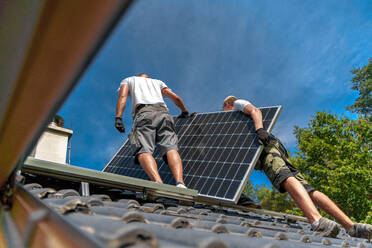 Männliche Arbeiter bei der Installation von Solarpaneelen auf einem Dach, alternative Energie, Ressourcenschonung und nachhaltiger Lebensstil. - HPIF03944