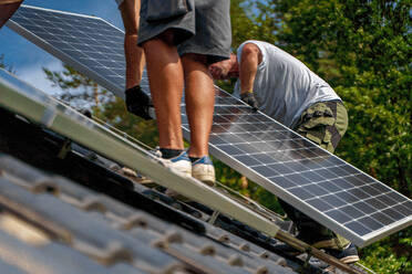 Männliche Arbeiter bei der Installation von Solarpaneelen auf einem Dach, alternative Energie, Ressourcenschonung und nachhaltiger Lebensstil. - HPIF03945