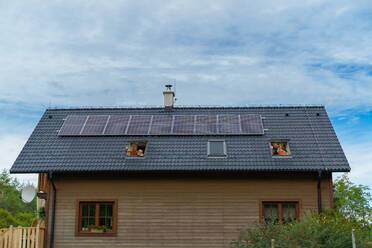 Eine glückliche Familie winkt aus den Dachfenstern ihres Hauses mit Sonnenkollektoren auf dem Dach. Alternative Energie, Ressourceneinsparung und nachhaltiger Lebensstil. - HPIF03949