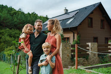 Glückliche Familie in der Nähe ihres Hauses mit Sonnenkollektoren. Alternative Energie, Ressourcenschonung und nachhaltiger Lebensstil. - HPIF03952