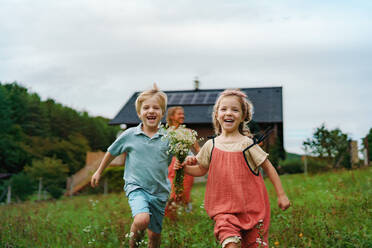 Glückliche Familie, die in der Nähe ihres Hauses mit einer Solaranlage läuft. Alternative Energie, Ressourcenschonung und nachhaltiges Lebenskonzept. - HPIF03973