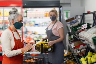 Eine junge und eine alte Verkäuferin füllen während einer Pandemie die Regale im Supermarkt auf. - HPIF03998