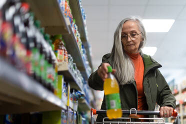 Ältere Seniorin, die im Supermarkt ein aromatisiertes Wasser kauft und auswählt. - HPIF04006