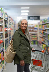 Eine ältere Frau steht und kauft im Supermarkt ein. - HPIF04008