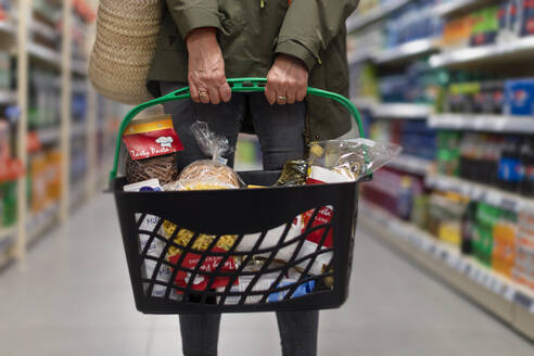Frau beim Einkaufen im Supermarkt, sie trägt einen vollen Einkaufskorb - HPIF04009