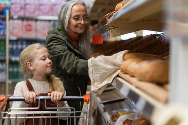 Großmutter mit ihrer Enkelin beim Aussuchen und Kaufen von Brot im Supermarkt. - HPIF04017