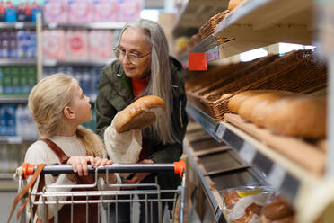 Großmutter mit ihrer Enkelin beim Aussuchen und Kaufen von Brot im Supermarkt. - HPIF04018