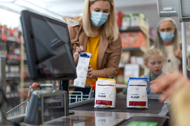 A young woman shopping in supermarket, putting products on checking desk during pandemic - HPIF04028