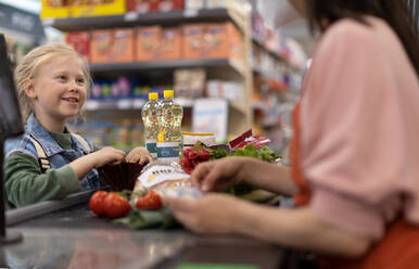 Close-up of a little blond girl paying for grocery shopping in supermarket. - HPIF04044