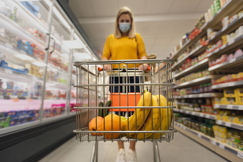 Eine junge Frau mit Gesichtsmaske und Einkaufswagen im Supermarkt, Inflationskonzept. - HPIF04053