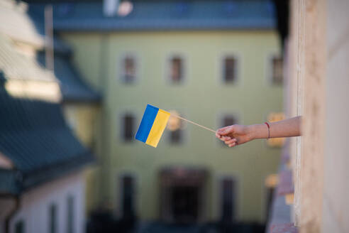 Die Hand eines Mädchens, das die ukrainische Flagge aus dem Fenster streckt - Solidarität mit der Ukraine im Krieg. - HPIF04066