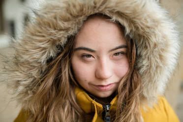 Eine Nahaufnahme einer jungen Frau mit Down-Syndrom, die eine Kapuze trägt und in die Kamera schaut - HPIF04078