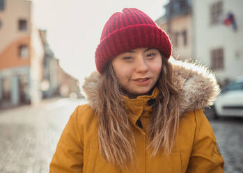 A happy young woman with Down syndrome weraing parka and hat, walking in town and looking at camera. - HPIF04082