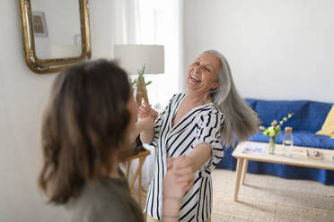 Eine glückliche ältere Großmutter mit einer Enkelin im Teenageralter, die gemeinsam zu Hause tanzen. - HPIF04123