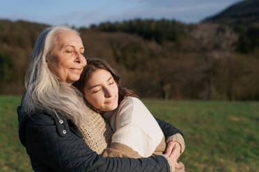 Eine glückliche ältere Großmutter mit Teenager-Enkelin umarmt in der Natur am Frühlingstag. - HPIF04129