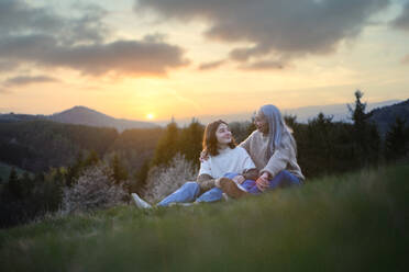 A happy senior grandmother with teenage granddaguhter sitting on grass in nature on spring day. - HPIF04132