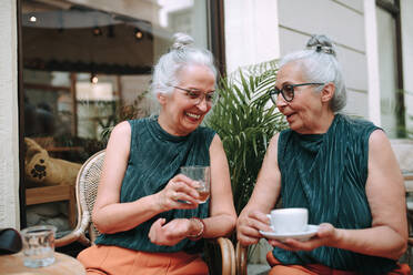 Happy senior women twins having a coffee break in city, smiling and talking. - HPIF04160