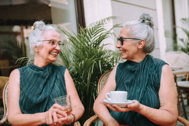 Happy senior women twins having a coffee break in city, smiling and talking. - HPIF04163