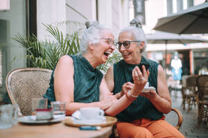 Glückliche ältere Frauen, die in der Stadt eine Kaffeepause machen, lächeln und sich unterhalten. - HPIF04165