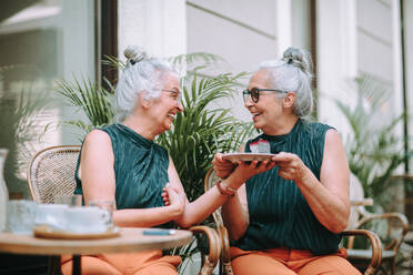 Happy senior women twins having a coffee break in city, smiling and talking. - HPIF04167