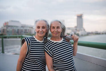 Portrait of happy seniors women, twins in the same clothes, walking on city bridge. - HPIF04186