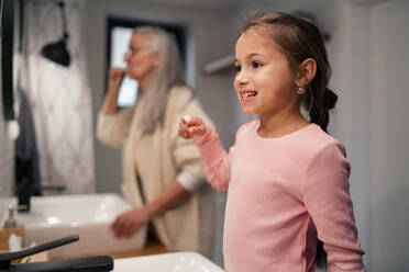 Eine ältere Großmutter und ihre Enkelin stehen im Badezimmer und putzen sich morgens die Zähne. - HPIF04212