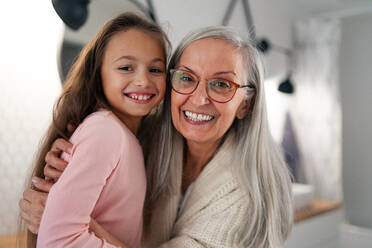 A senior grandmother and granddaughter standing indoors in bathroom, hugging and looking at camera. - HPIF04215