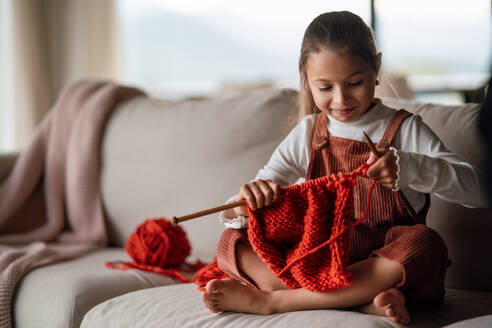 Ein kleines Mädchen sitzt auf dem Sofa und lernt zu Hause stricken. - HPIF04238