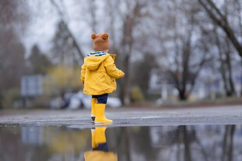 Fröhlicher kleiner Junge springt in Pfütze nach regen in kalten Herbsttag. - HPIF04264