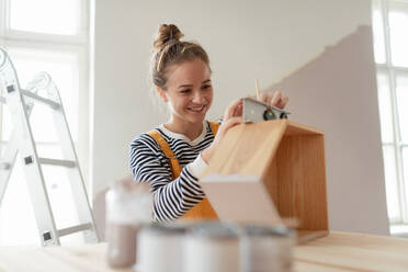 Porträt einer jungen Frau, die ein Regal in ihrem Haus neu einrichtet. Konzept der Wiederverwendung von Materialien und des nachhaltigen Lebensstils. - HPIF04269
