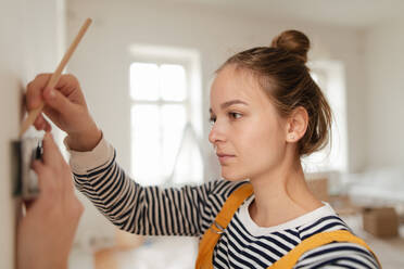 Young woman remaking her apartment, measuring wall with spirit level and hanging a shelf. - HPIF04272